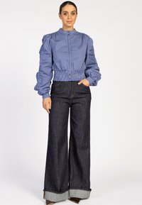 Blauw en wit gestreepte crop-jack met puffmouwen en een aansluitende tailleband, gecombineerd met hoogopgetrokken donkere denim wijde broek met een omslag.