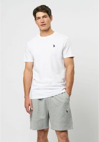 Balta medvilninė marškinė su trumpomis rankovėmis, puošta maža juoda logotipu. Sujungta su pilkomis medvilninėmis šortais, abi yra patogios ir laisvalaikio stiliaus.