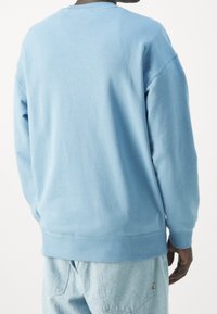 Sudadera azul claro con cuello redondo, puños y dobladillo acanalados. Material suave, corte relajado, con una textura lisa y un diseño minimalista.