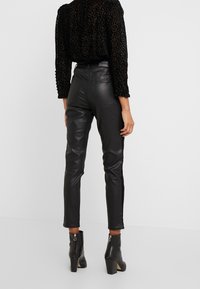 Zwarte leren broek met een smalle pasvorm en zijkstreepdetails, gecombineerd met een gestructureerde zwarte top met luipaardprint en enkellaarzen.