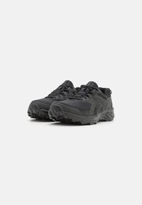 Zapatillas deportivas negras con parte superior de malla, suela de goma texturizada, puntera reforzada y sistema de cordones. Cuenta con una marca en el lateral.