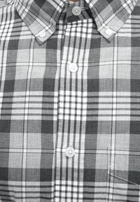 Chemise à carreaux noir et blanc avec boutons blancs et col boutonné.