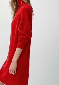 Rode gebreide jurk met een hoge halslijn, lange mouwen en een losse pasvorm. De textuur is geribbeld en de stof lijkt zacht en dik.