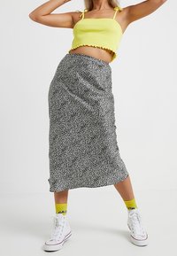 Gul kort topp med volangkant, kombinerad med svart-vit prickig medellång kjol och vita sneakers med gula accenter.