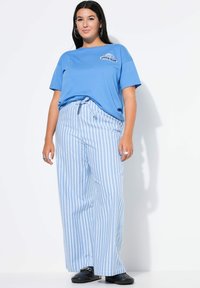 Modré tričko s nápisem "DREAM TEAM" v kombinaci s vysokým pasem a širokými pruhovanými kalhotami v světle modré a bílé barvě. Černé boty.