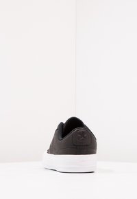 Sneaker nera in tela con suola in gomma, dotata di un pannello posteriore testurizzato e di un accento con logo. Design piatto e profilo basso.