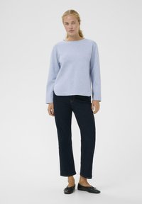 Hele sinine ümmarguse kaelusega pusa, kombineeritud tumesiniste sirgete teksapükstega ja mustade madalate kingadega. Sile kangas, minimaalsete detailidega.