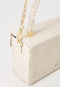 Beige krokodillepræget håndtaske med en struktureret design, der har en tekstureret overflade, guldfarvet hardware og en aftagelig kædderem.