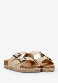 Sandalias beige con dos correas ajustables con hebillas, una parte superior texturizada y una suela de corcho trenzado. Presenta un diseño troquelado para ventilación.