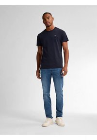 Camiseta de algodón azul marino con cuello redondo y un pequeño logo, combinada con vaqueros de mezclilla azul claro y zapatillas blancas.