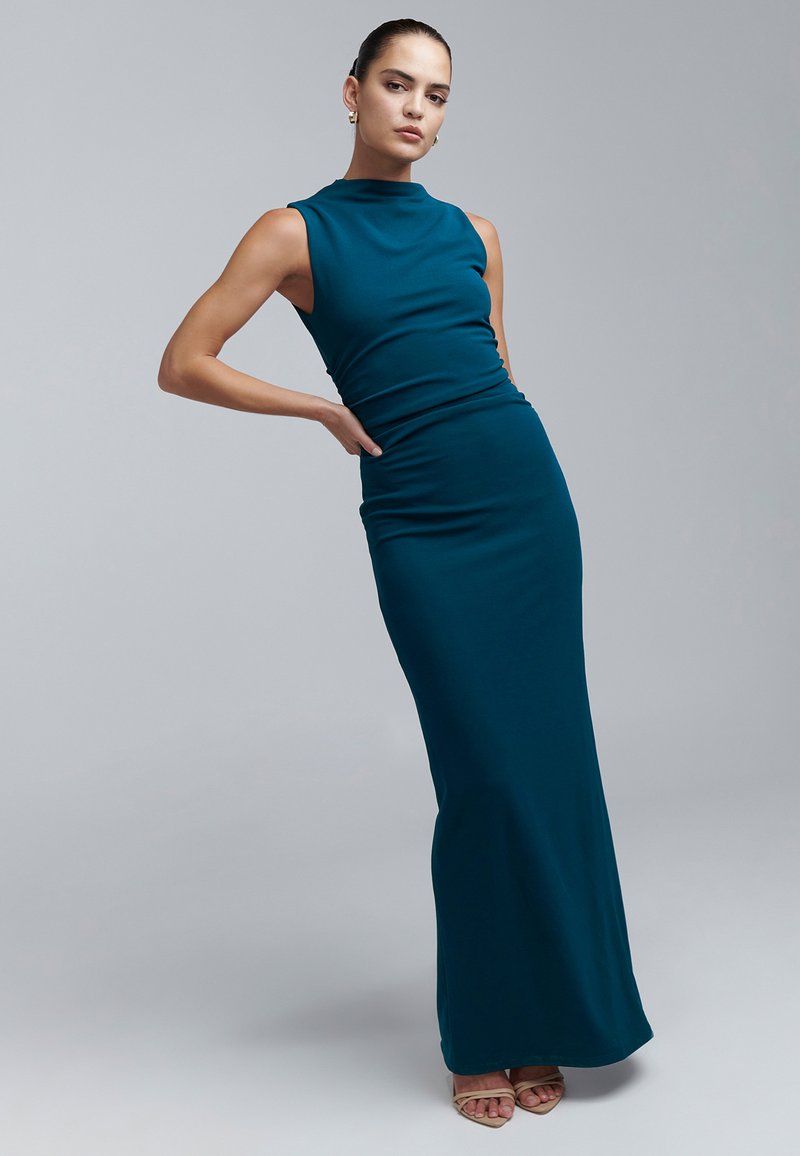 Turkooizen mouwloze jurk met een hoge halslijn en een aansluitend silhouet, gemaakt van gladde stof, reikt tot de vloer. Minimalistisch ontwerp, zonder patronen.