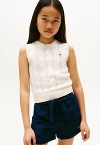 Haut sans manches blanc avec un motif en maille texturé, associé à un short bleu marine avec une ceinture en tissu et des poches latérales.
