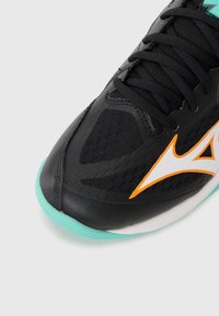 Black athletic shoe with a mesh upper, turquoise sole, and orange accents. Features prominent lacing and streamlined design elements.