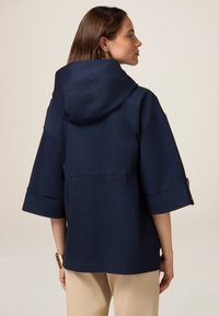 Chaqueta con capucha azul marino de diseño holgado, mangas cortas y puños enrollados. Tejido suave con una silueta simple y limpia.