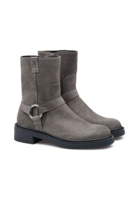 Bottines en suède gris avec une texture lisse, dotées d'un accent métallique circulaire sur la sangle et d'une semelle en caoutchouc noir. Fermeture éclair sur le côté.