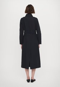 Tumesinine trench coat vöökohaga, pikad varrukad ja selja lõhik liikumiseks. Omab klassikalist kraed ja siledat kangatekstuuri.