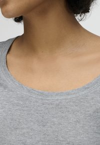 Area del collo e della clavicola di una persona che indossa una maglietta grigio chiaro a girocollo con tessuto strutturato.