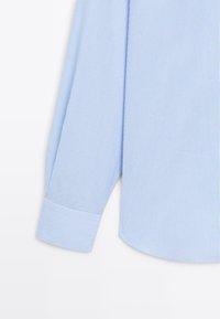 Hellblau gestreiftes Langarmhemd mit kontrastierendem Bündchen; der Stoff wirkt glatt mit schmalen vertikalen Streifen, die durchgehend sind.