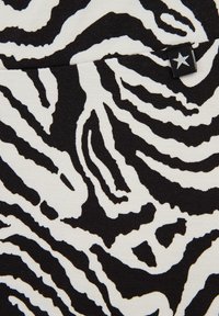 Svart och vit zebramönstrad tyg som har djärva, vågiga linjer. Materialet är stretchigt med en subtil textur. En liten svart etikett med en vit stjärna finns närvarande.