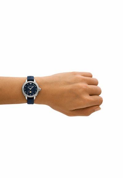 Reloj redondo con esfera de color azul marino, caja y bisel plateados. Correa de silicona texturizada en azul marino. Cuenta con tres subesferas y acentos brillantes.