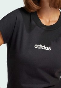 Black short-sleeved t-shirt made of cotton, featuring a round neckline and a white "adidas" logo centered at the chest.