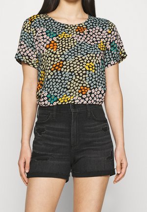 Woman wearing a multicolored small floral print short-sleeve blouse and high-waisted black distressed denim shorts.