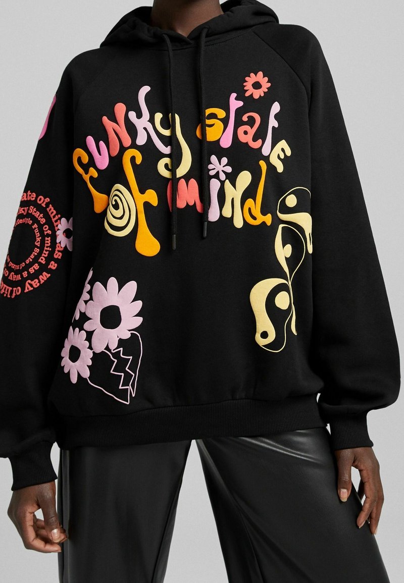 Musta huppari, jossa on värikäs graafinen painatus, sisältäen tekstiä ja kukkakuvioita vaaleanpunaisena, keltaisena ja oranssina. Hupussa kiristysnauha ja ribbineulotut hihansuut.