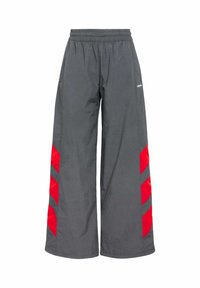 Sive široke hlače s elastičnim pojasom koje imaju odvažne crvene chevron uzorke sa stranica. Napravljene su od laganog, glatkog materijala.