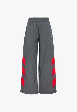 Graue Schlaghosen mit einem elastischen Bund, die markante rote Chevron-Akzente an den Seiten aufweisen. Hergestellt aus leichtem, glattem Material.