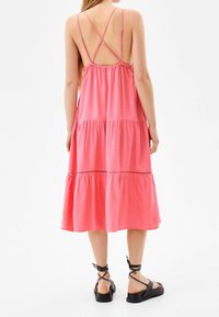 Rosa ärmlös klänning med ett lagerdesign, med öppen rygg och korskorsade axelband. Matchas med svarta sandaler med remmar.