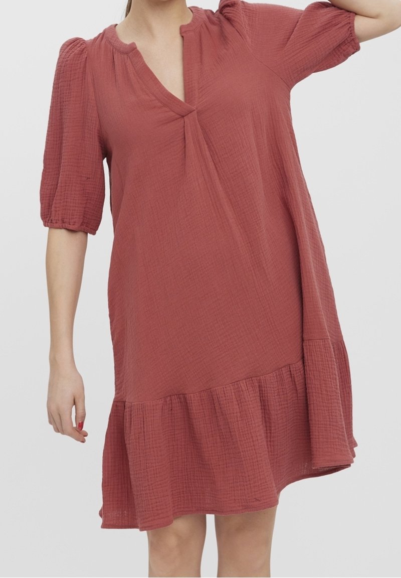 Robe couleur rouille, longueur genou, en tissu texturé froissé. Elle présente un décolleté en V, des manches courtes bouffantes et un ourlet évasé avec des volants.