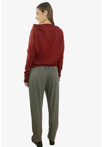 Czerwony top z długim rękawem i odkrytymi plecami, zestawiony z oliwkowozielonymi spodniami o szerokich nogawkach. Gładka tkanina o luźnym kroju z subtelnym detalem kieszeni.