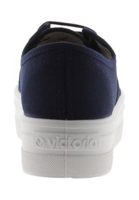 Mörkblå kanvas sneakers med vit gummisula, sedd bakifrån med "Victoria"-logotyp präglad på hälen.
