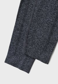 Tumedates hallid spordilegendi, mis on valmistatud tekstuurilisest kangast, millel on sile vöökoht ja peened vertikaalsed õmblused lisadeatnikuks.