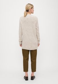 Beige strikket genser med ribbestrikket søm, sett fra baksiden, kombinert med olivengrønn avkortet bukse og mørke sko, som viser en myk tekstur og avslappet passform.