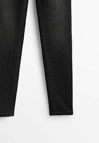 Jean slim noir avec coutures visibles sur fond blanc, montrant la moitié inférieure des jambes du pantalon.