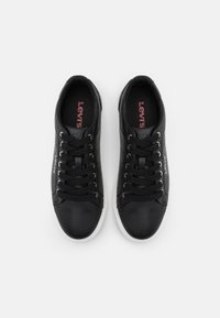 Crne kožne tenisice s bijelim gumenim đonom, okruglim prstima i crnim vezicama. Imaju crveni "Levi's" logo na ulošcima i minimalistički dizajn.