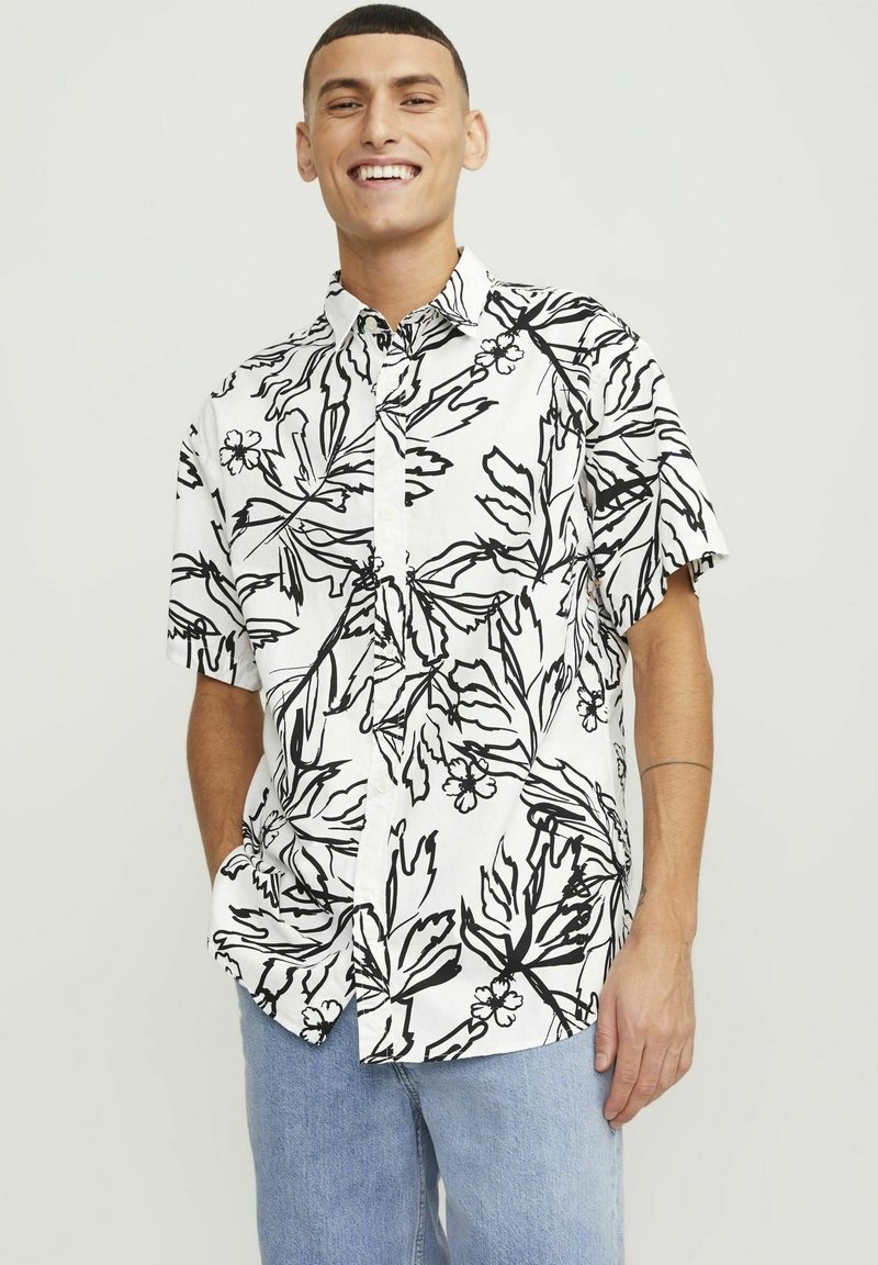Chemise à manches courtes blanche, ornée d'un motif floral noir. Fermeture à bouton sur le devant avec une coupe décontractée, fabriquée en tissu léger.