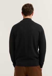 Maglione nero a maglia esposto nella parte posteriore, con maniche lunghe, scollo tondeggiante e una texture liscia. Completato con un orlo aderente.