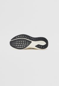 Semelle en caoutchouc noire avec un motif texturé comprenant des découpes, des bords arrondis et une semelle intermédiaire blanche. Design léger pour une meilleure adhérence.