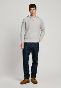 Heledad hallhall, millel on tõmblukuga krae, koos tumedate teksade ja helepruunide lipsudega saabastega. Lihtne, mugav riietus.