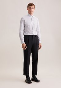 Witte button-up shirt met kleine blauwe stippen, gecombineerd met op maat gemaakte zwarte broeken en zwarte leren schoenen. Gladde stof, klassieke pasvorm.