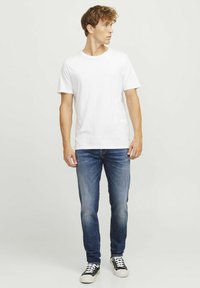 Bijela pamučna majica u kombinaciji s plavim farmerkama. Outfit nadopunjuju crno-bijele tenisice, što pokazuje ležeran stil.