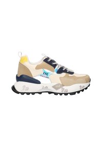 Zapatilla gruesa en color beige, blanco y marino con acento en el talón amarillo, cordones con patrón y suela gruesa texturizada que lleva el nombre de la marca "EXÉ".