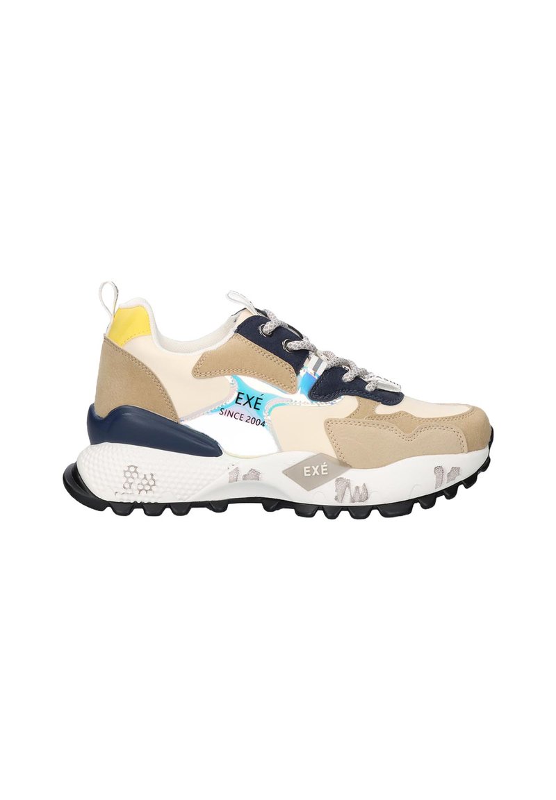 Zapatilla gruesa en color beige, blanco y marino con acento en el talón amarillo, cordones con patrón y suela gruesa texturizada que lleva el nombre de la marca "EXÉ".