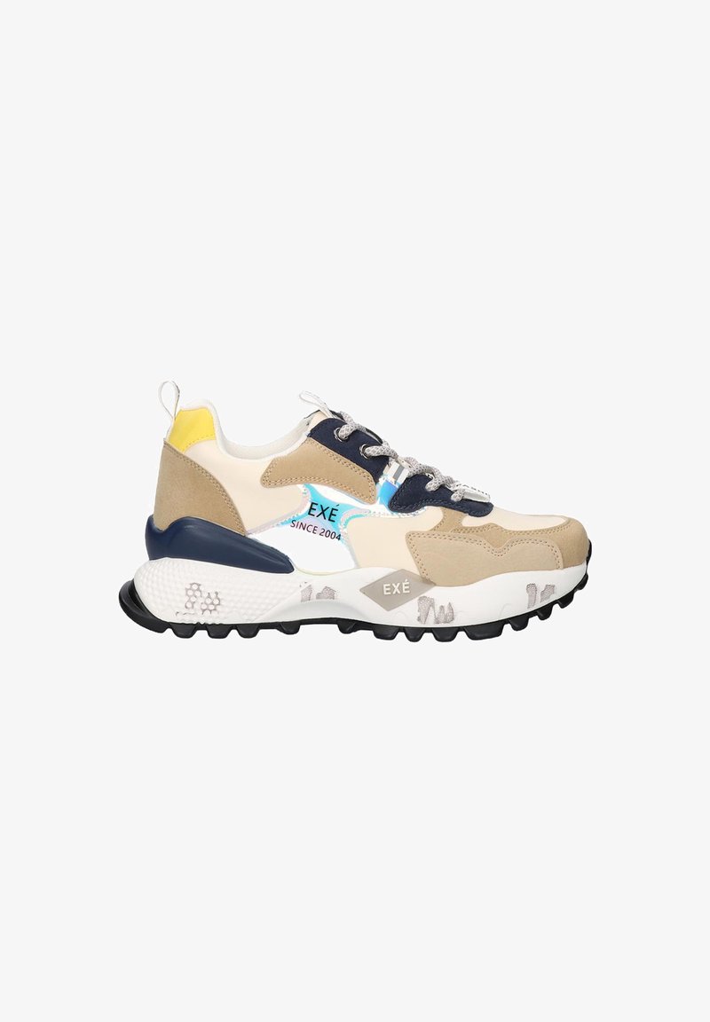 Zapatilla gruesa en color beige, blanco y marino con acento en el talón amarillo, cordones con patrón y suela gruesa texturizada que lleva el nombre de la marca "EXÉ".