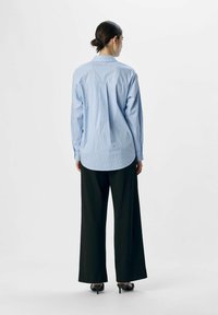 Blauw-wit gestreepte overhemden met lange mouwen, een ronde onderkant en een relaxte pasvorm, gecombineerd met zwarte wijde broek.
