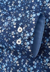 Hemd mit blauem Blumenmuster auf dunkelblauem Hintergrund. Verfügt über hellblaue Akzente, Knopfmanschetten und zwei weiße Knöpfe an der Manschette.