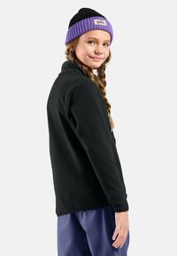 Giacca in pile nera con colletto alto e berretto lavorato a maglia con dettagli in viola. I dettagli includono un'etichetta tessuta sul cappello e una texture liscia.