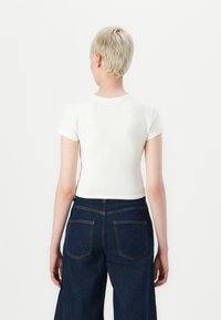 Hvit cropped t-skjorte med korte ermer, kombinert med mørkeblå høyt midje jeans med baklommer og en klassisk denimtekstur.
